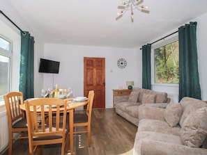 A dining area with a wooden table and chairs, a sofa, a TV mounted on the wall, and a window with curtains.