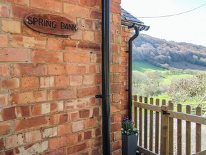 A brick wall with a 'SPRING BANK' sign, a wooden fence, and a view of a green landscape.