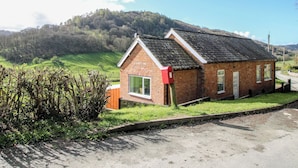 A small brick house with a sloped roof, a mailbox, and a grassy yard. - Spring Bank (Llanfyllin)