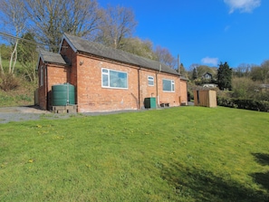 A brick house with a large window, a green water tank, and a grassy yard. - Spring Bank (Llanfyllin)