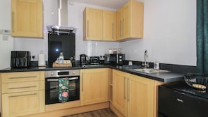 A kitchen with wooden cabinets, a stainless steel range hood, a black refrigerator, and a microwave. - Spring Bank (Llanfyllin)