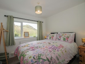 A bedroom with a bed, a window with curtains, a bedside lamp, and a wooden dresser.
