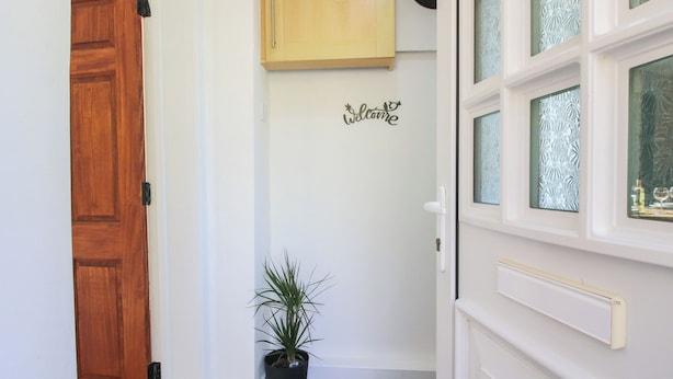 A hallway with a wooden door, a potted plant, a welcome sign, and frosted glass windows. - Spring Bank (Llanfyllin)