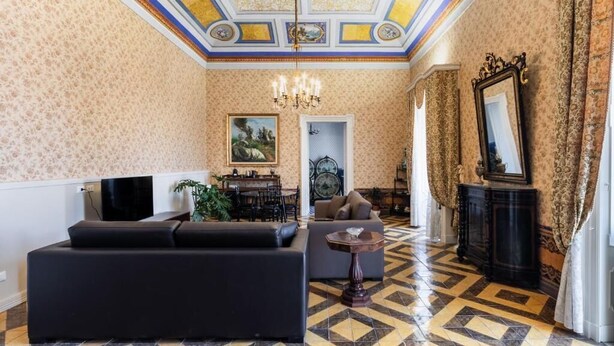 Una habitación con papel tapiz estampado, un candelabro, un sofá, una mesa de comedor y un espejo.