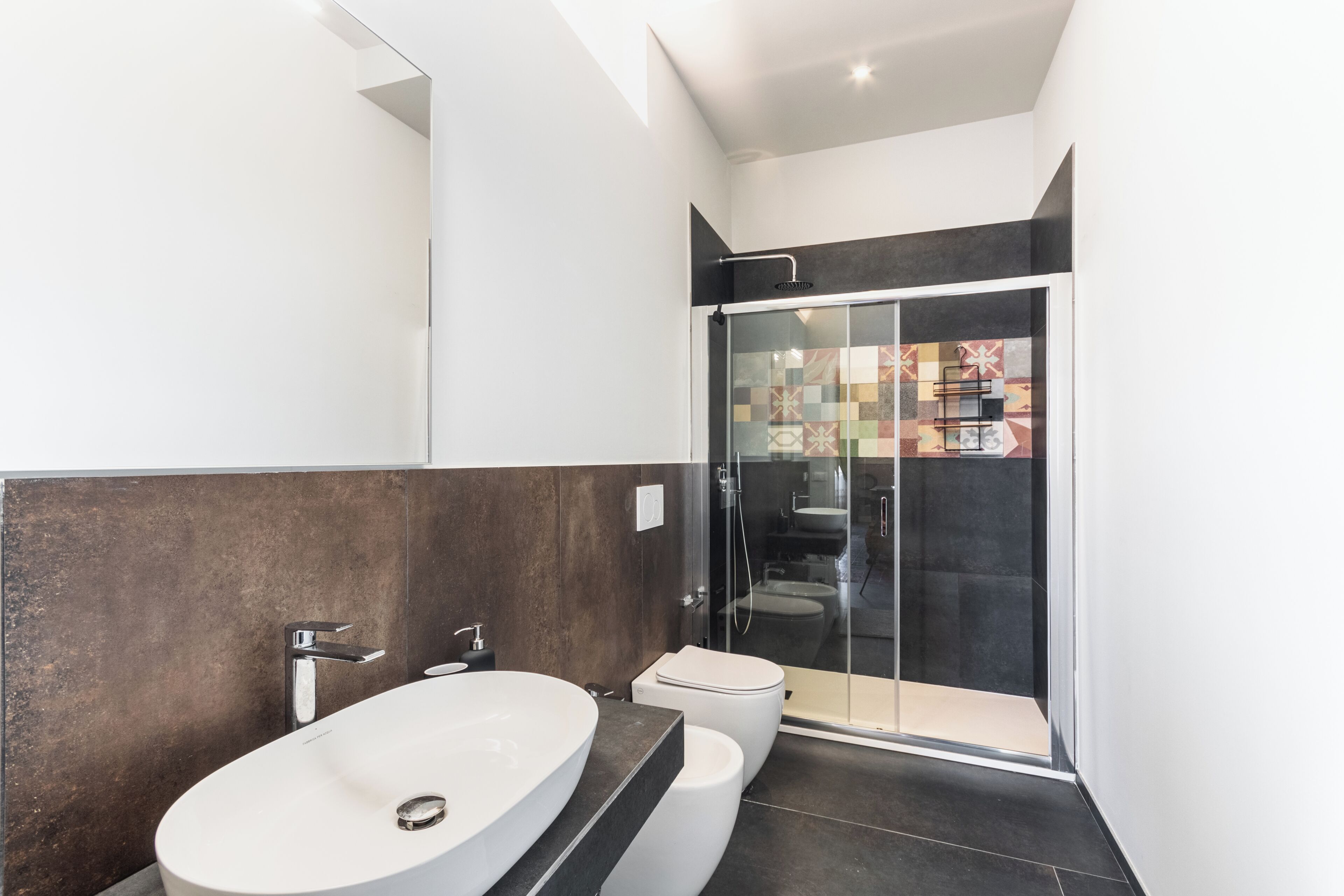 A modern bathroom with a large oval sink, a toilet, and a glass-enclosed shower.