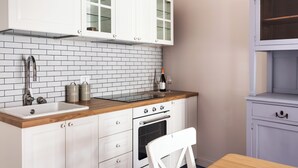 Una cocina con armarios blancos, encimera de madera, un fregadero, un horno y una botella de vino.