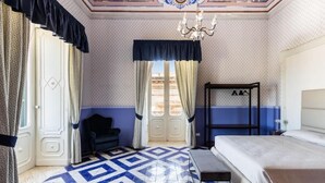 Habitación de hotel con piso de diseño geométrico, cama, banco, silla, armario y candelabro.
