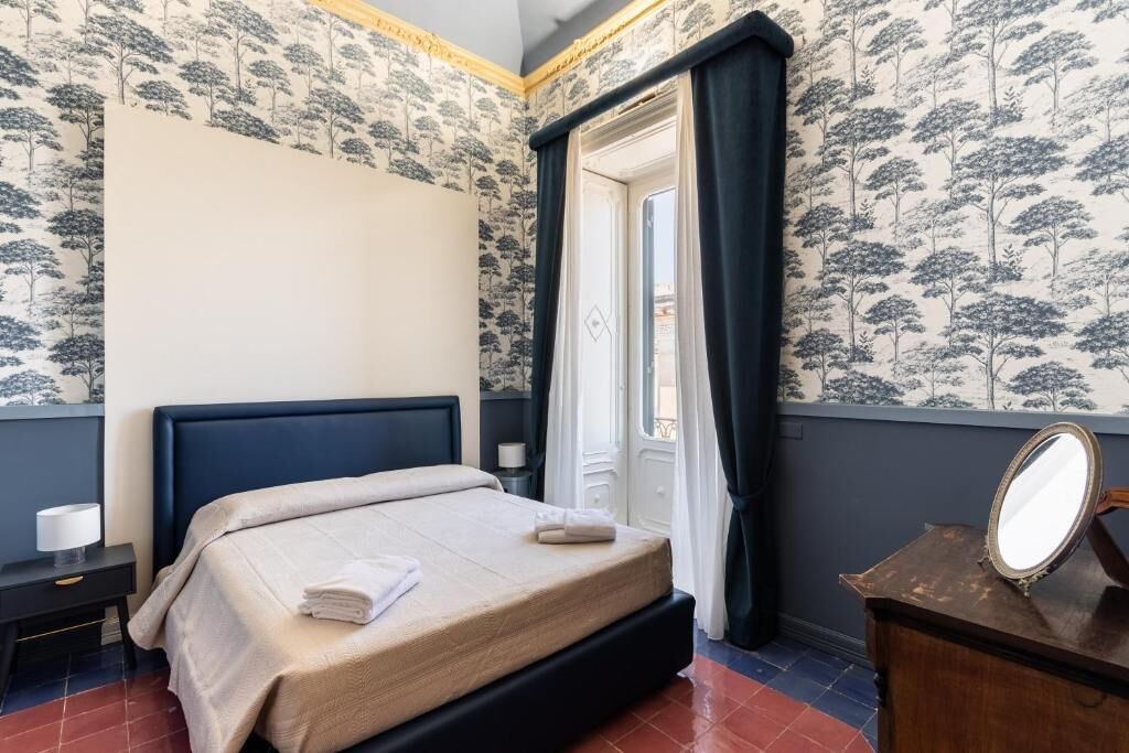 A hotel room with a bed, a nightstand, a dresser, a mirror, and a window with curtains.