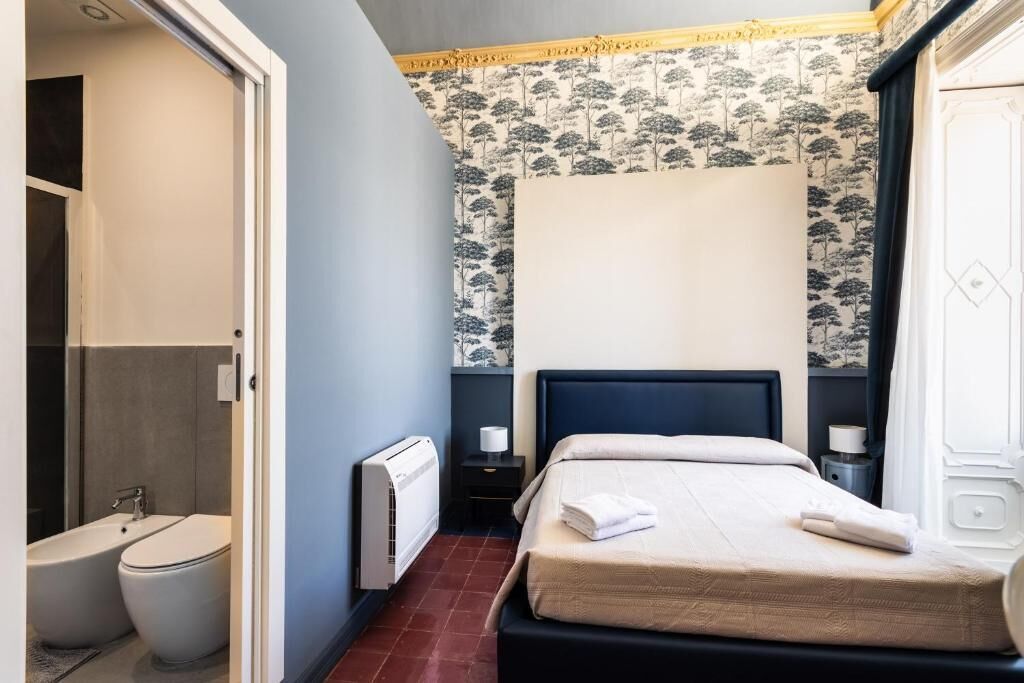 Un dormitorio con cama, mesita de noche, radiador y baño con inodoro y bidé.