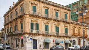 Un edificio histórico de estilo arquitectónico clásico, con fachada simétrica, varios balcones y una serie de ventanas con contraventanas.