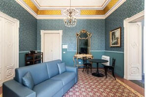 Une pièce avec un canapé bleu, une table à manger avec des chaises, un miroir et un lustre.