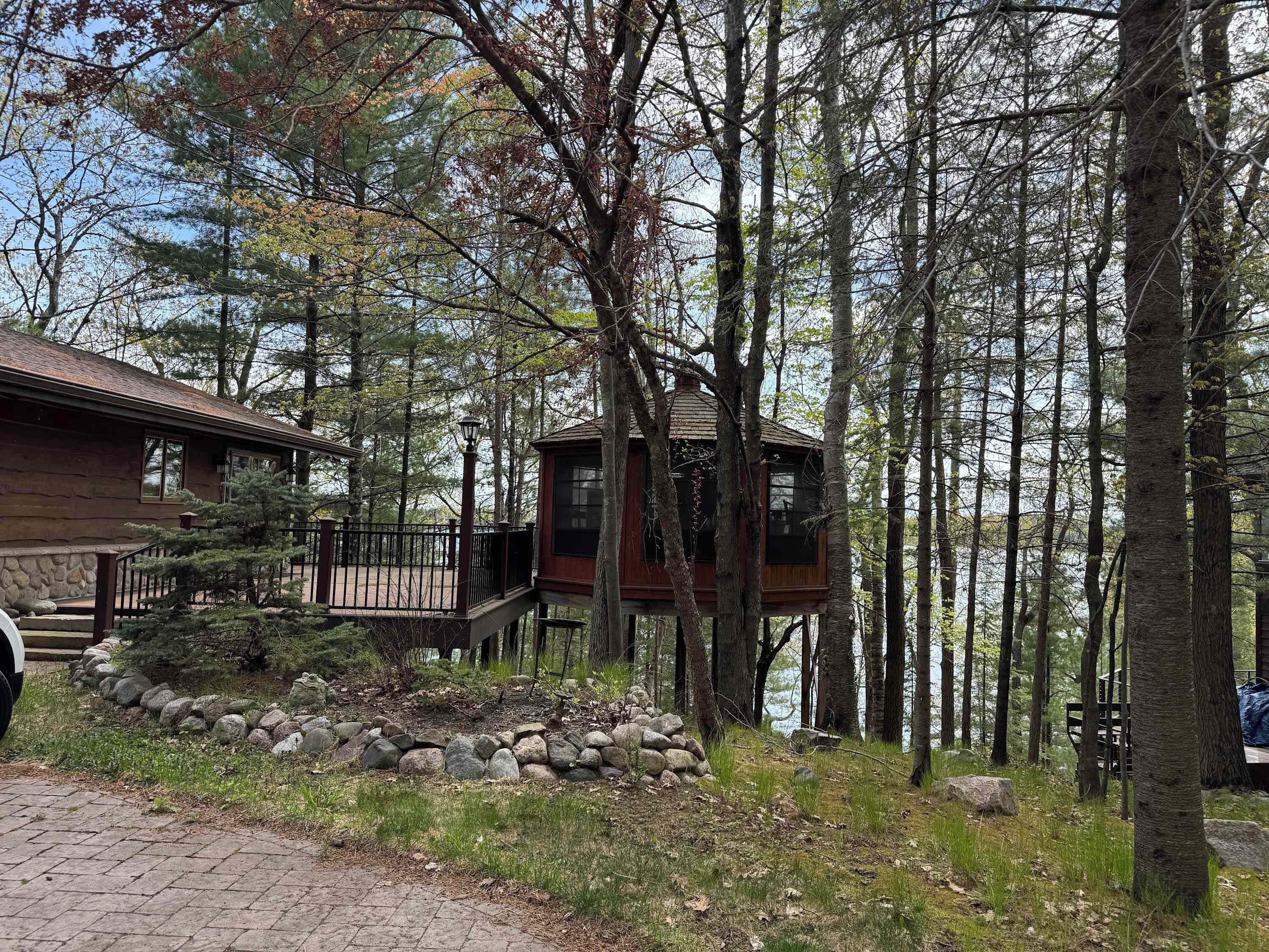A cabin with a deck, surrounded by trees and a stone wall.