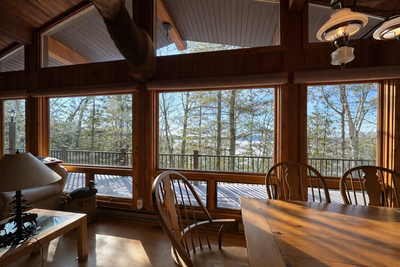 A wooden interior with large windows, a dining table, chairs, and a lamp.