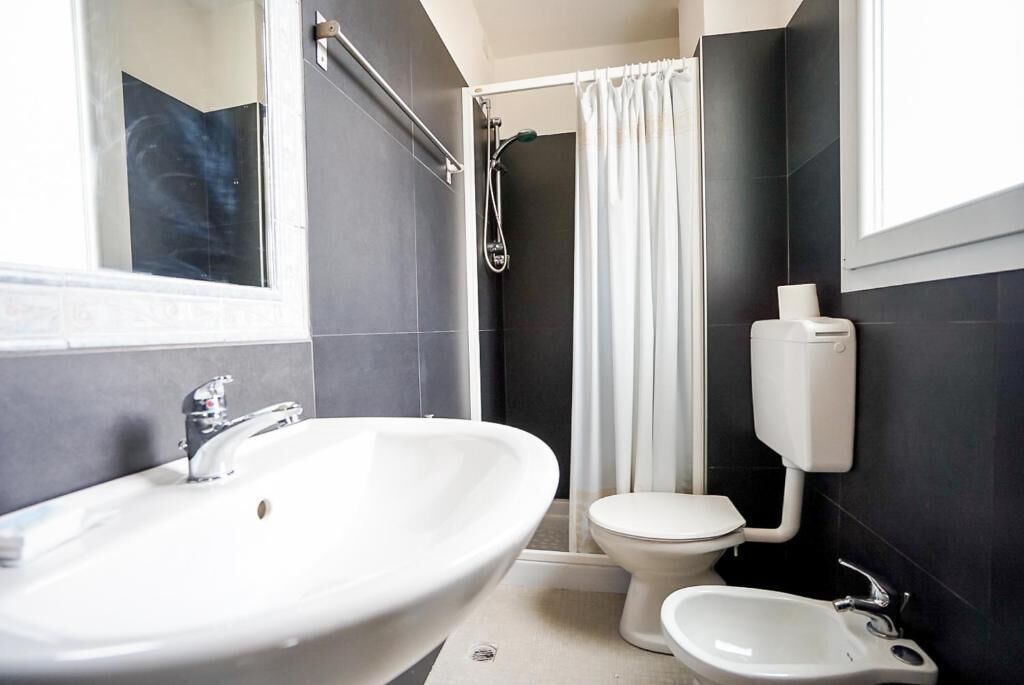 Ein Badezimmer mit einem großen weißen Waschbecken, einer Toilette, einem Bidet und einer Duschkabine mit Vorhang.