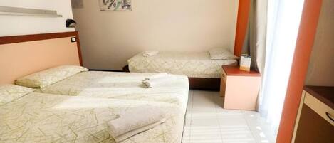A hotel room with two beds, a small table, a nightstand, a poster on the wall, and a window with curtains.