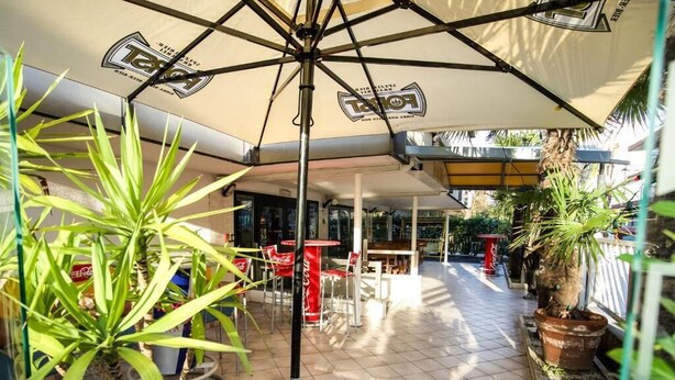 A covered outdoor area with tables and chairs, potted plants, and a Coca-Cola sign. - hotel elba (Rivazzurra)