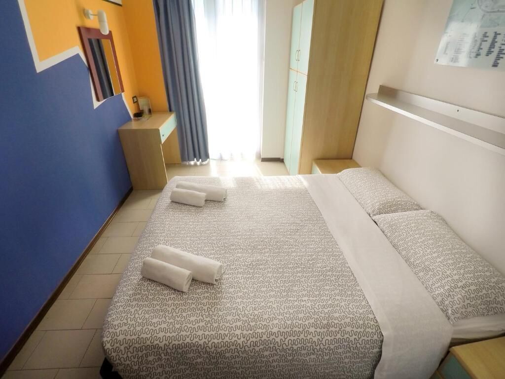 Una camera d'albergo con un letto, una scrivania, un armadio e una finestra con tende.