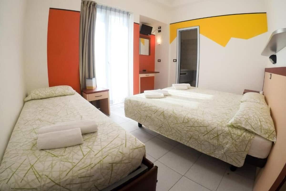 A hotel room with two single beds, a bathroom, and a mirror.