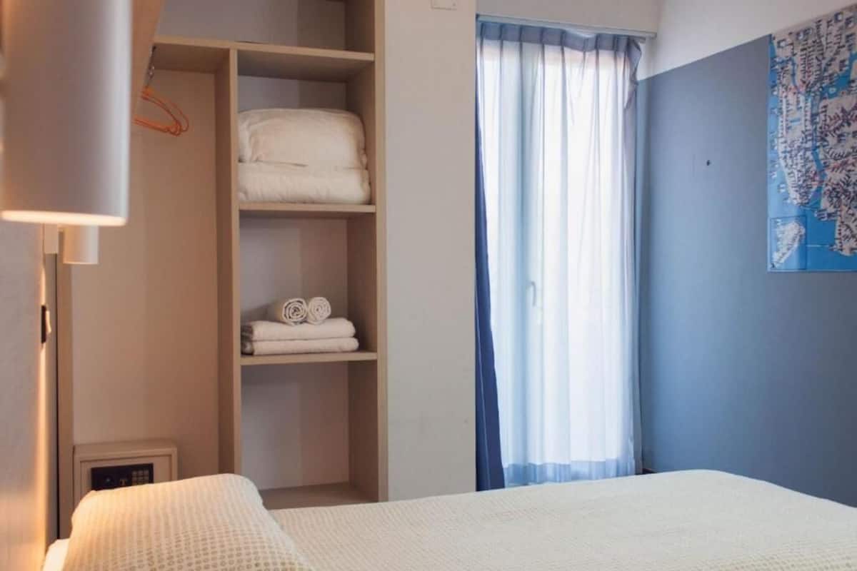 A hotel room with a bed, a wardrobe, and a window with curtains.