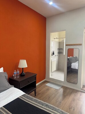 A hotel room with a bed, a nightstand with water bottles, a mirror, and a shower area. - Private Studio Near Condesa, Roma & Chapultepec (Ciudad de México)