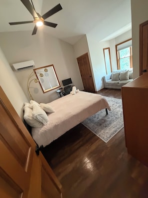A bedroom with a bed, a ceiling fan, an air conditioning unit, a desk with a chair, a television, and a window with blinds. - Elegant Lakefront Escape - Boat Slip + Two-Story Deck - Sleeps 10 - Pet Allowed (Greentown)