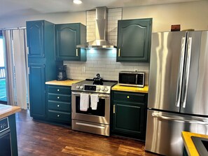 A modern kitchen with dark green cabinets, stainless steel appliances, and a wooden countertop.