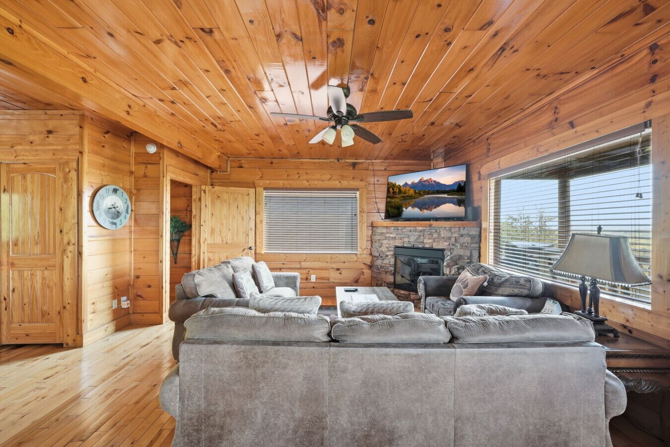 Interior acolhedor de uma cabana, com teto de madeira, lareira, sofá e televisão.