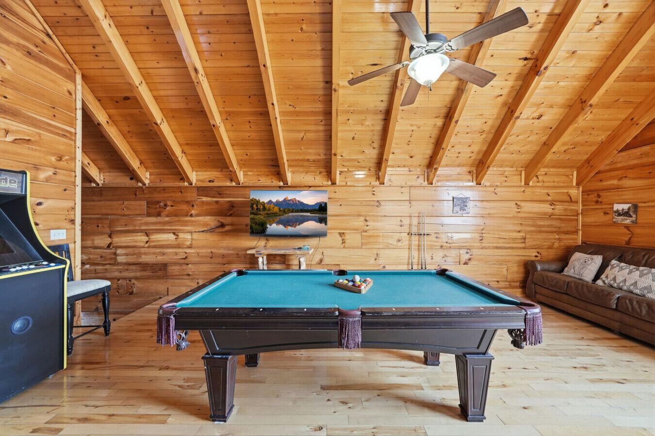 A pool table in a wooden room with a ceiling fan, a couch, and a framed picture on the wall.