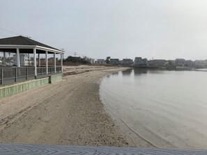 Ein Strand mit einer überdachten Struktur, einem sandigen Ufer und Wohnhäusern im Hintergrund.