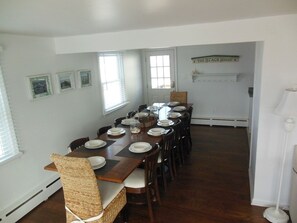 A dining room with a long table set for six, framed pictures on the wall, and a sign reading 'The Beach House'. - Ocean side 6 houses to the beach; 4 bed with full SUNSET views (Beach Haven)