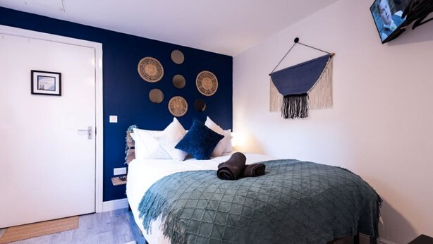 Ein Schlafzimmer mit einem Bett, Kissen, einer Decke, einem an der Wand montierten Fernseher und einer Tür.