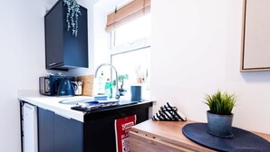 Eine kleine Küche mit Spüle, Kaffeemaschine, einer Pflanze und einem Brandschutznachweis.