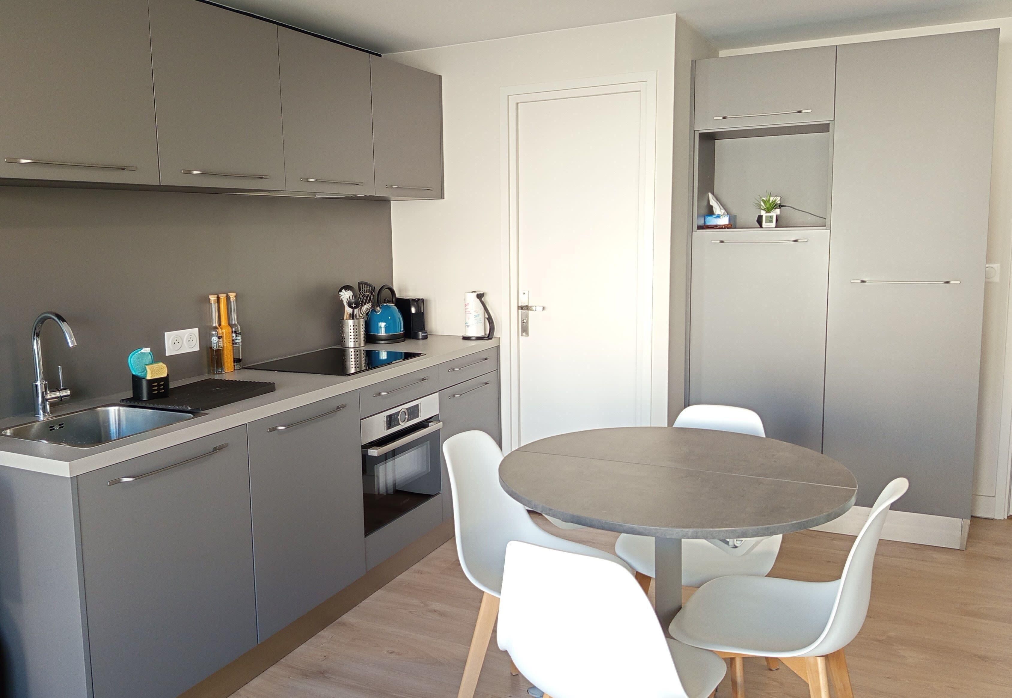 Een moderne keuken met grijze kastjes, een spoelbak en een ronde tafel met stoelen.