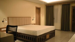 Een hotelkamer met een bed, een bureau, een stoel, een nachtkastje, een lamp, een deur en een raam met gordijnen.