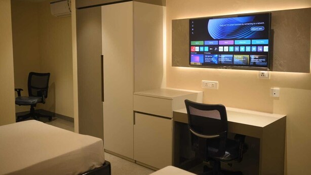 Een hotelkamer met een bureau, een stoel, een bed en een tv aan de muur waarop verschillende apps worden getoond.