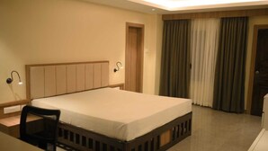 Een hotelkamer met een bed, een bureau, een stoel, een nachtkastje en een raam met gordijnen.