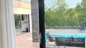A modern living room with a large sliding glass door leading to a pool area.