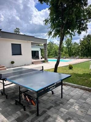 Mesa de ping pong al aire libre con una casa moderna de fondo.