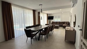 A modern living room with a dining area, a sofa set, a TV, and a small table.