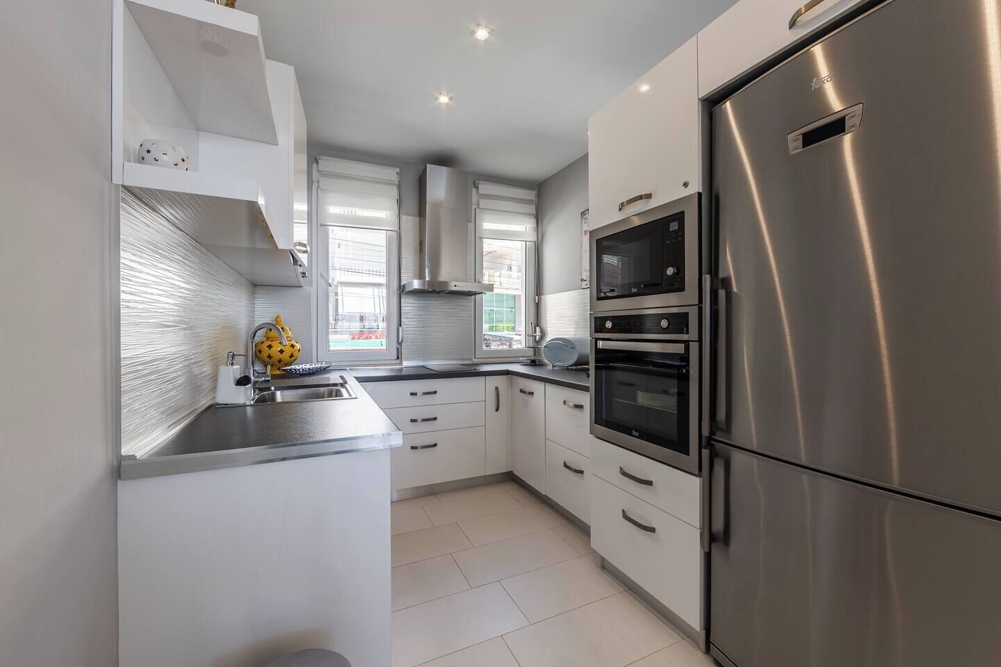 A modern kitchen with stainless steel appliances, white cabinetry, and a large window providing natural light.