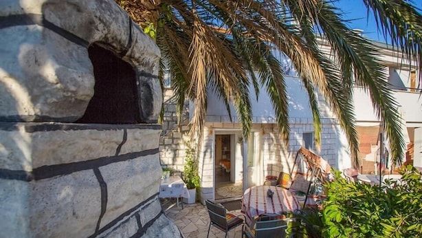 A stone wall, a patio with a table and chairs, and a building in the background. - Holiday Home Katica in Okrug Gornji (Okrug Gornji)