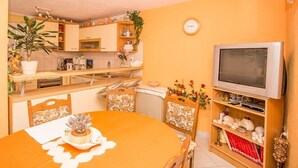 A compact kitchen with a dining area, a television, and a clock on the wall. - Holiday Home Katica in Okrug Gornji (Okrug Gornji)