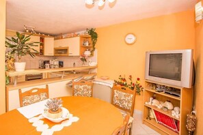 Een kleine keuken met een eethoek, een televisie en een klok aan de muur.