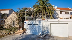 A residential building with a garage, a stone house, and a palm tree. - Holiday Home Katica in Okrug Gornji (Okrug Gornji)