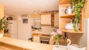 A kitchen with white cabinets, a microwave, a stove, and a sink. There are potted plants and a vase with flowers on the counter. - Holiday Home Katica in Okrug Gornji (Okrug Gornji)