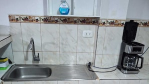Una cucina con lavello, una moka e una bottiglia di sapone per le mani sul piano di lavoro.