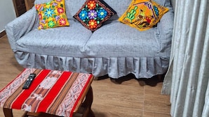 Un divano grigio con cuscini colorati, una panca di legno con un cuscino decorato e un pavimento in legno.