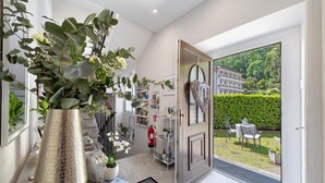 A modern interior with a large metallic vase, a bookshelf, and a view of a well-maintained garden through an open door.