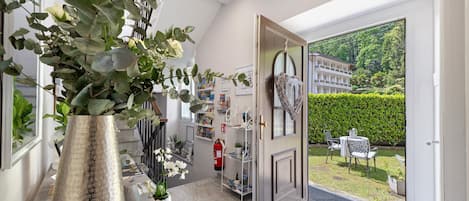 A modern interior with a large metallic vase, a bookshelf, and a view of a well-maintained garden through an open door.
