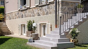 A stone building with a set of stone steps leading to a door, a metal railing, and potted plants.